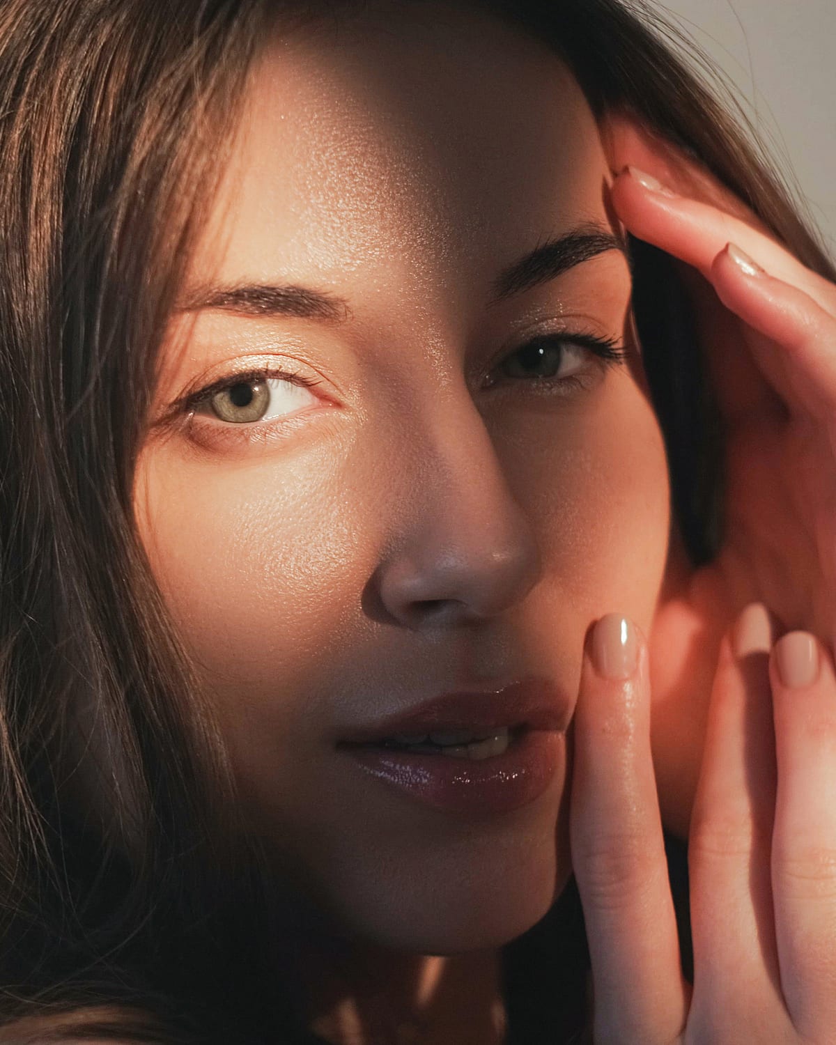 A model resting her fingertips on her cheek in warm side light