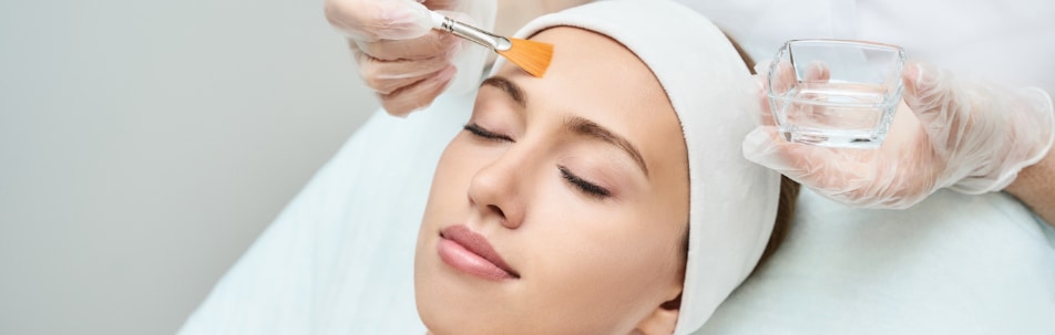 Woman with eyes closed having a chemical peel solution brushed onto her forehead