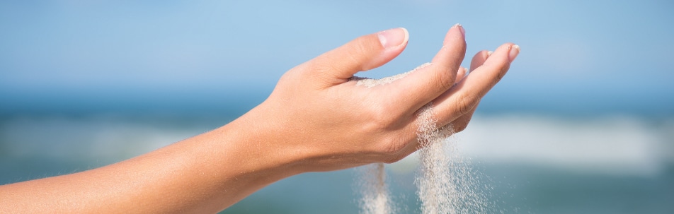 Woman's hand letting sand run through her fingers in front of the sea