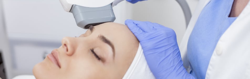 Woman lying back with eyes closed as a light therapy device is held near her forehead