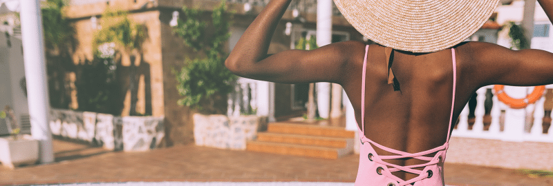 Stock photograph of a woman seen from behind in a straw hat and pink swimsuit outdoors