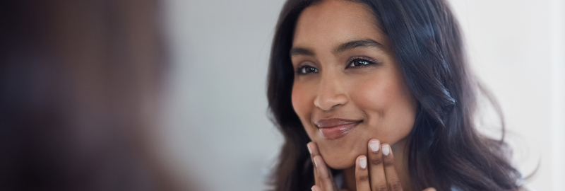 Stock photograph of a smiling woman touching her chin, looking at her reflection in a mirror