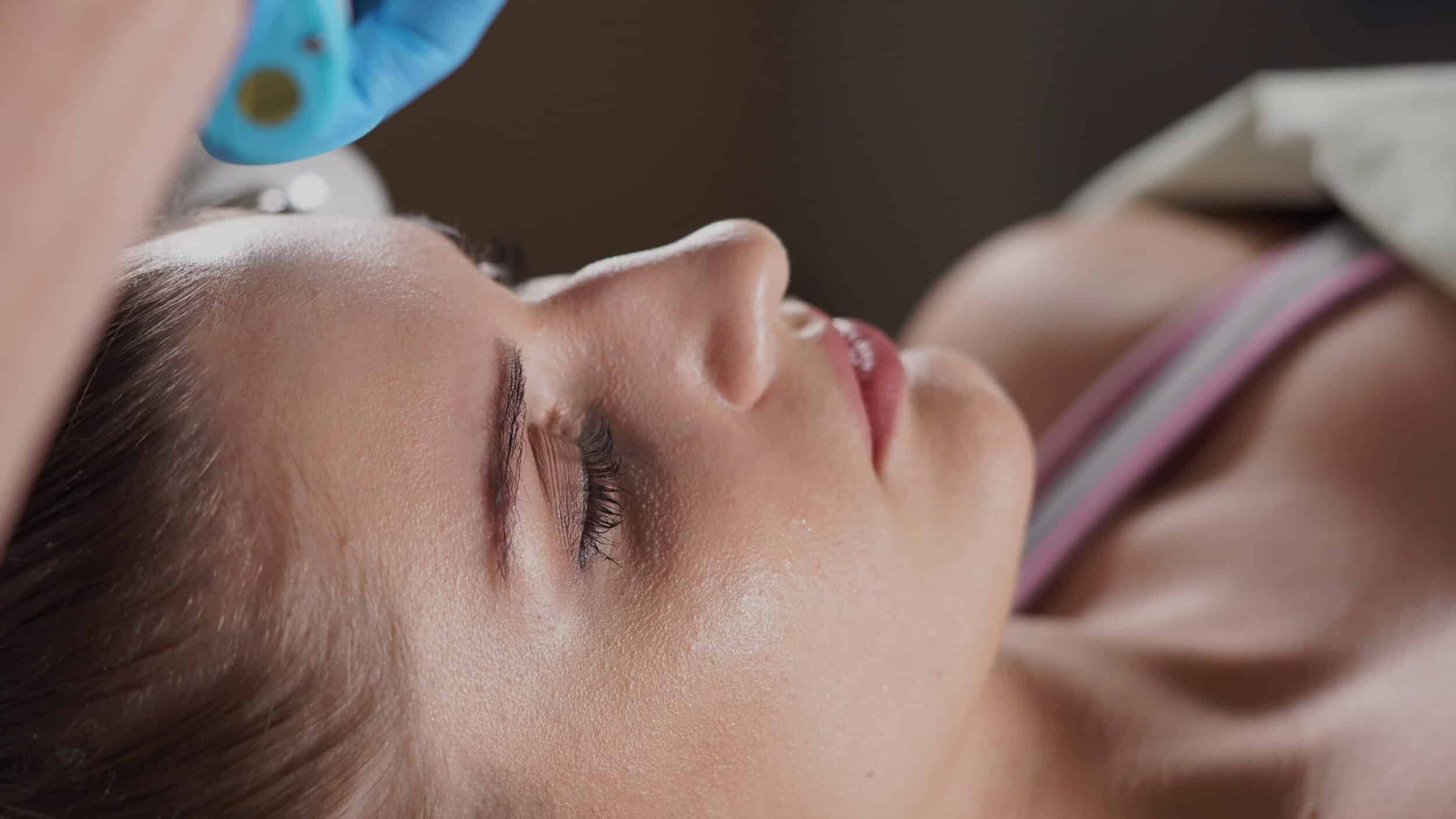 Stock photograph of a model lying back with her eyes closed during a facial treatment, a gloved hand at her temple